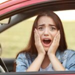 donna in auto con espressione scioccata e le mani sulle guance