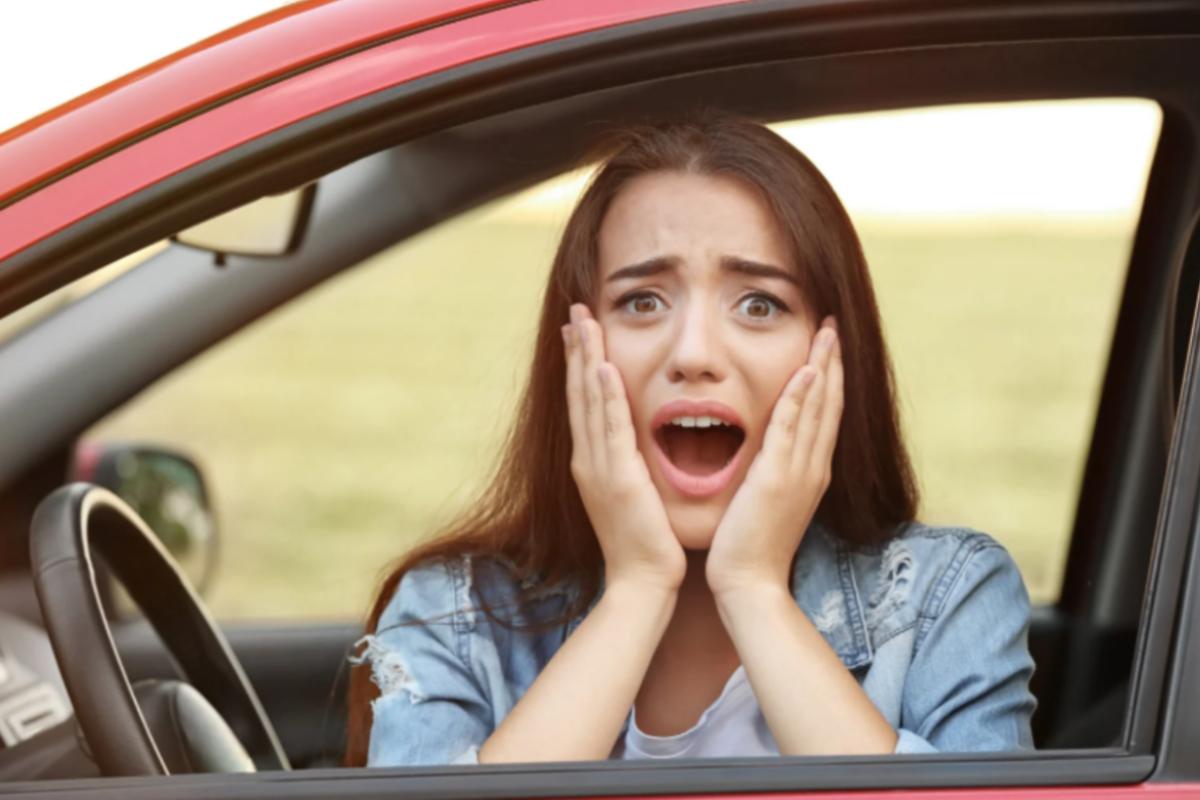 donna in auto con espressione scioccata e le mani sulle guance
