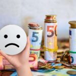 sfondo banconote e monete euro e mano con sagoma faccina triste