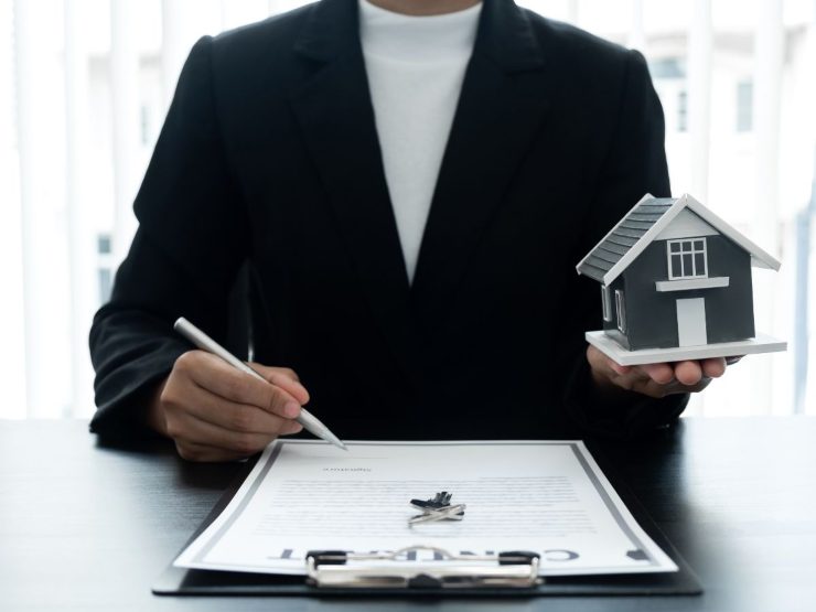 persona alla scrivania firma documento con casetta in miniatura in mano